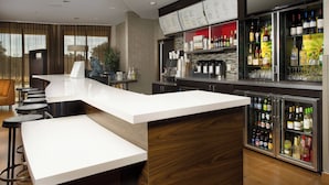 A modern bar area with a white countertop, stools, and a refrigerator stocked with beverages. - Courtyard by Marriott San Antonio Lackland (San Antonio)