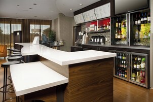 Eine moderne Bar mit einer weißen Arbeitsplatte, Hockstühlen und einem mit Getränken gefüllten Kühlschrank.