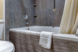 A modern bathroom with a freestanding bathtub, a toilet, and a shower curtain. - Econo Lodge & Suites Southern Pines - Pinehurst (Southern Pines)