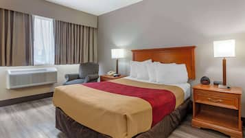 Habitación de hotel con una cama grande, dos mesitas de noche con lámparas, una silla, una ventana con cortinas y un equipo de aire acondicionado.