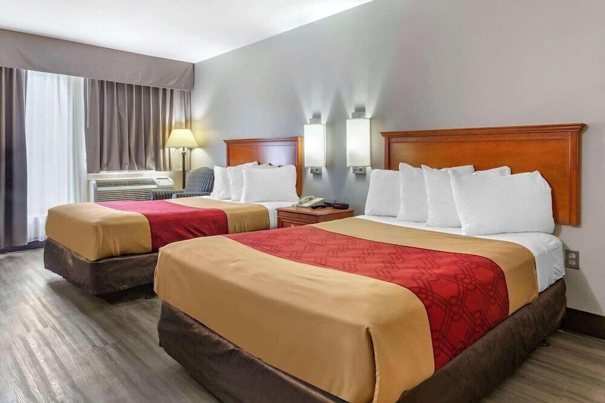 A hotel room with two beds, a desk, a lamp, and a window with curtains.