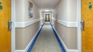 A hotel hallway with doors numbered 109 and 112, a patterned carpet, and a corridor leading to a door at the end. - Econo Lodge & Suites Southern Pines - Pinehurst (Southern Pines)
