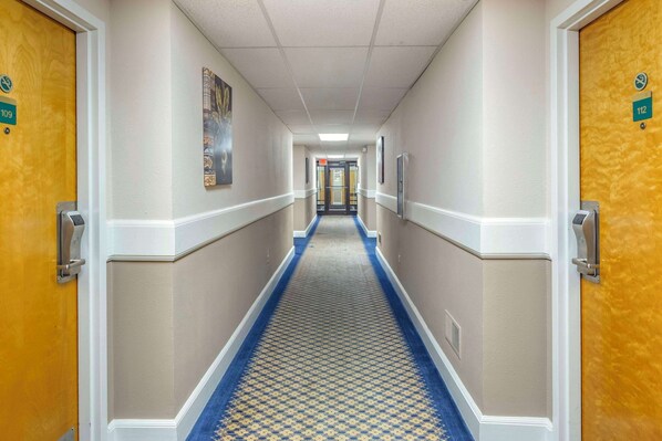 A hotel hallway with doors numbered 109 and 112, a patterned carpet, and a corridor leading to a door at the end. - Econo Lodge & Suites Southern Pines - Pinehurst (Southern Pines)