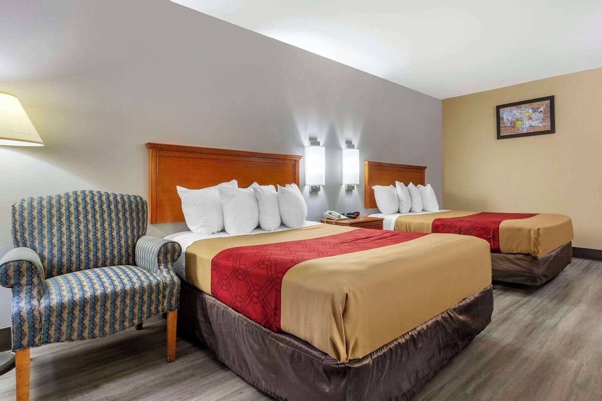 A hotel room with two beds, a chair, and a nightstand.