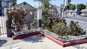 A gated area with a white picket fence, a small building, and a street with a white pickup truck. - Value Inn Bellflower (Bellflower)