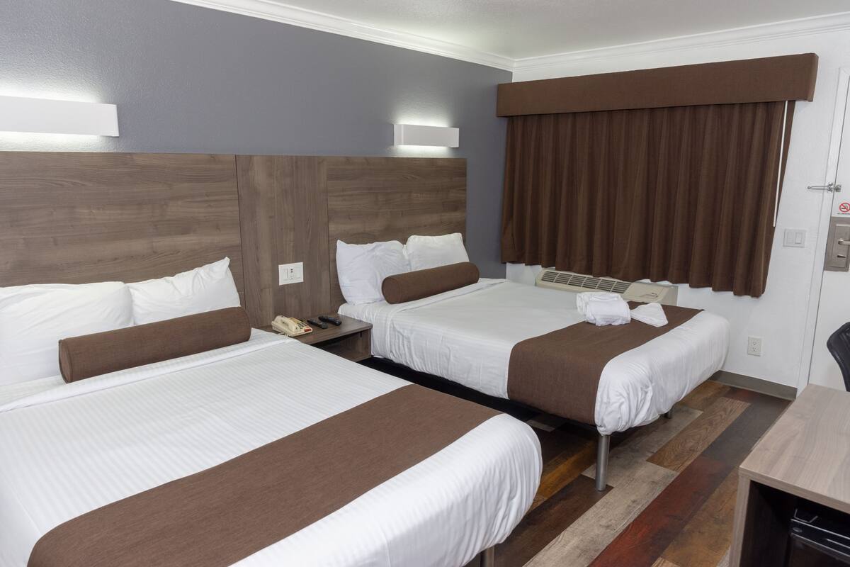 Quarto de hotel com duas camas, uma mesa e uma cadeira.