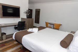 A hotel room with a bed, a desk with a chair, a TV mounted on the wall, and a mirror.