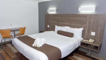 A hotel room with a large bed, a bedside table with a phone, a chair, and a desk.