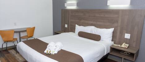 A hotel room with a large bed, a bedside table with a phone, a chair, and a desk.