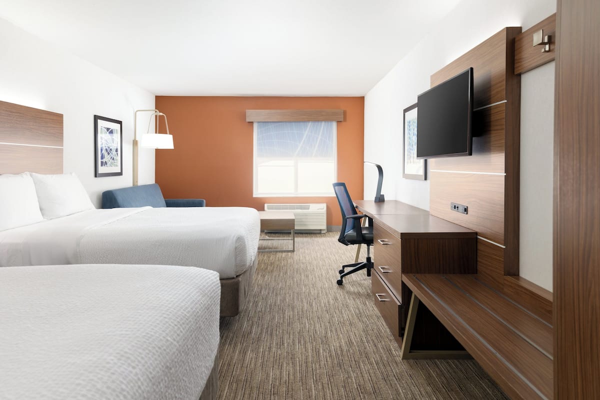 A hotel room with two beds, a desk, a chair, a television, and a window with blinds.