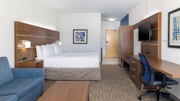 A hotel room with a bed, a desk with a chair, a sofa, a TV, and a framed picture on the wall.