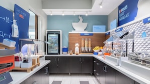A modern breakfast area with a self-serve station, a refrigerator, and a variety of food options.