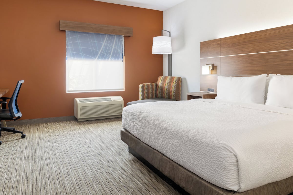 A hotel room with a large bed, a chair, a desk, and a window with blinds.