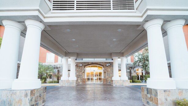 A building entrance with a covered walkway, columns, and a stone facade.