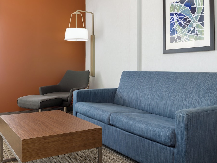 A modern living room with a blue sofa, a wooden coffee table, a floor lamp, and a framed abstract painting on the wall.