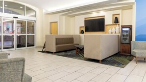 A hotel lobby with a seating area, a television, a reception desk, and a glass door entrance.