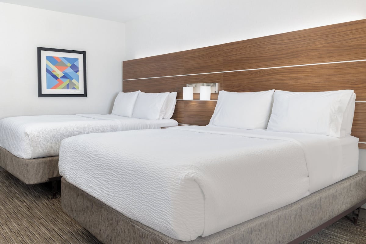 A hotel room with two beds, a wooden headboard, a framed abstract painting, and a nightstand with a lamp.