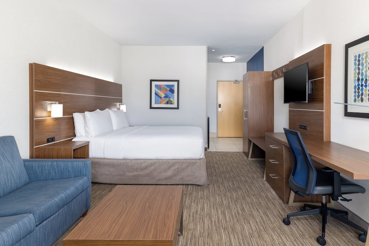 A hotel room with a bed, a desk with a chair, a sofa, a TV, and a framed picture on the wall.
