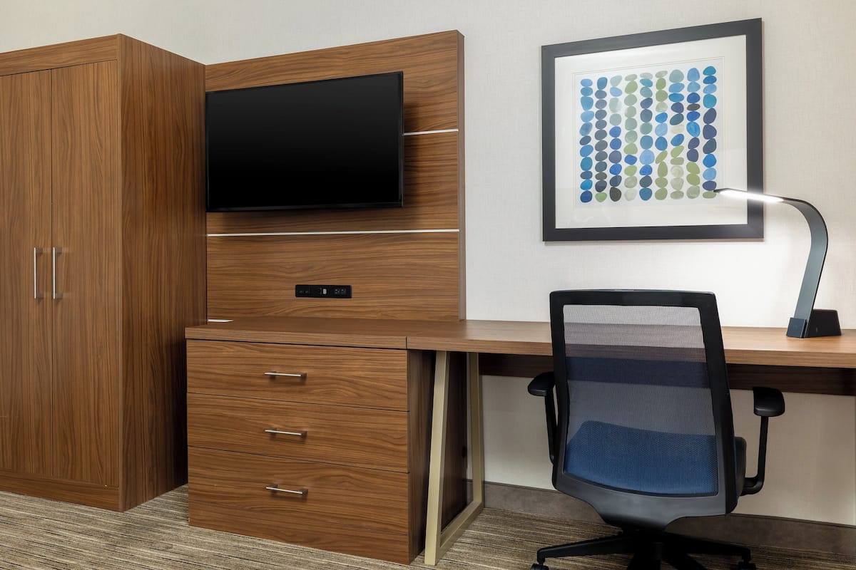A modern office space with a wooden desk, a mounted TV, a framed artwork, and a computer setup.