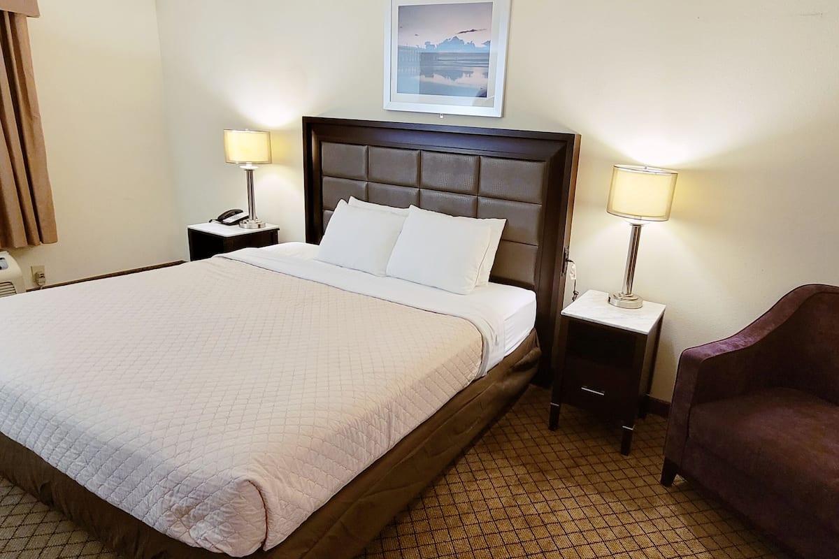 A hotel room with a large bed, two bedside tables with lamps, a chair, and a wall-mounted picture.