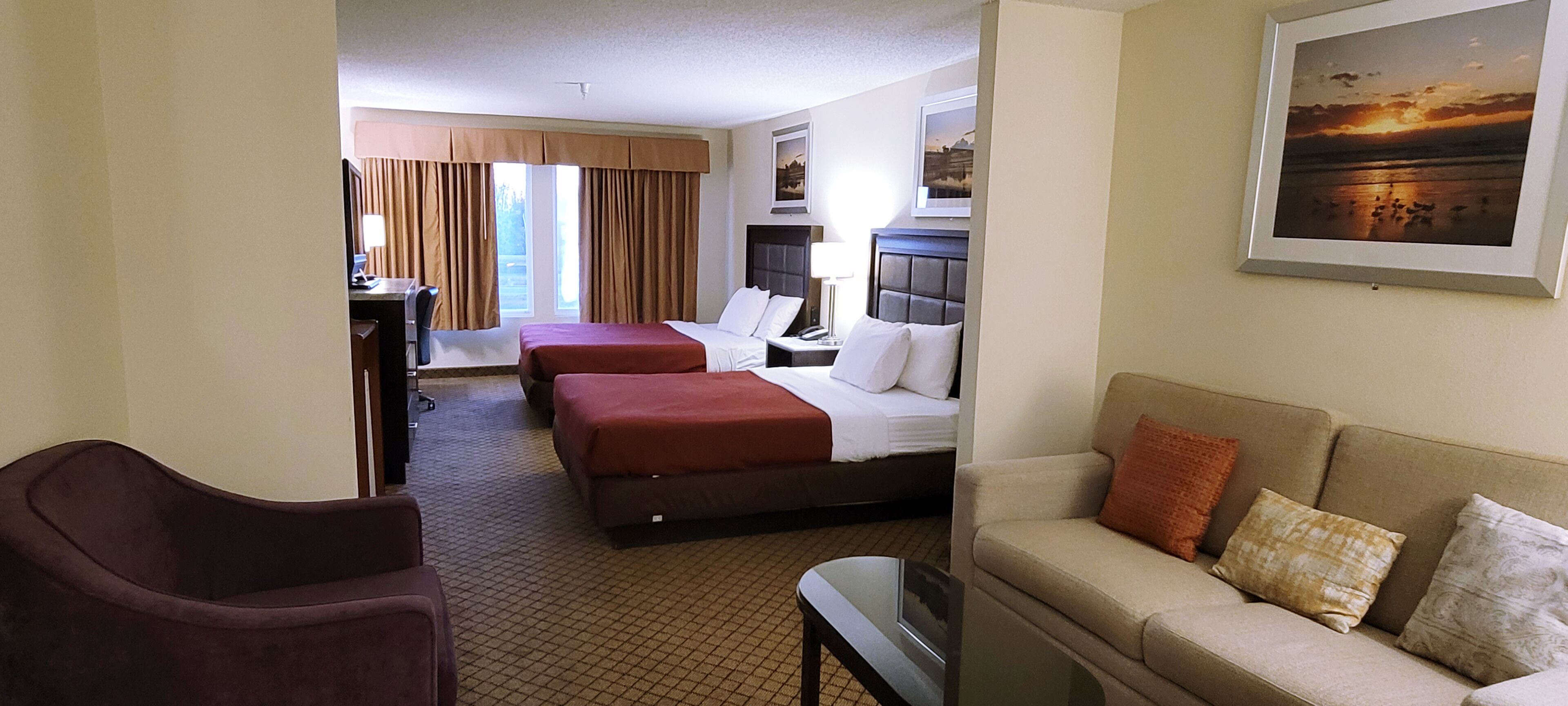 Ein Hotelzimmer mit zwei Betten, einer Sitzecke, einem Schreibtisch und einem Fernseher.