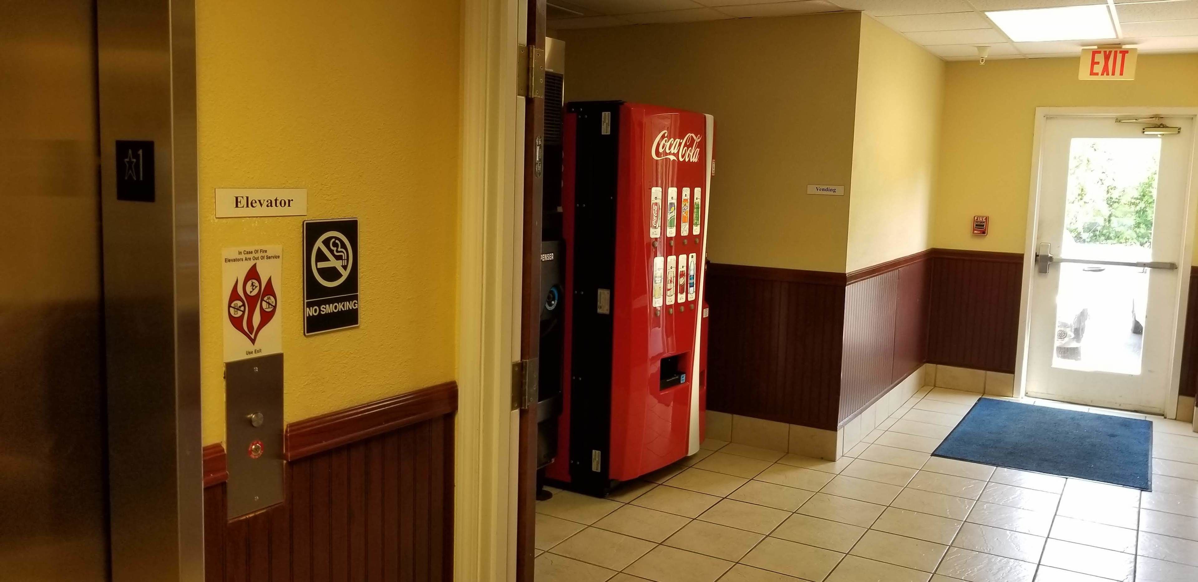 A hallway with a vending machine, a Coca-Cola machine, an elevator, and a door marked "EXIT".
