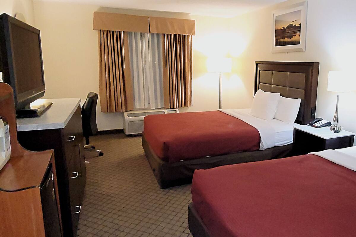A hotel room with two beds, a desk with a television, a lamp, and an air conditioning unit.