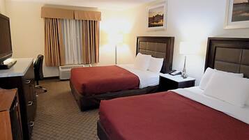 Quarto de hotel com duas camas, uma escrivaninha com televisão, uma luminária e ar condicionado.