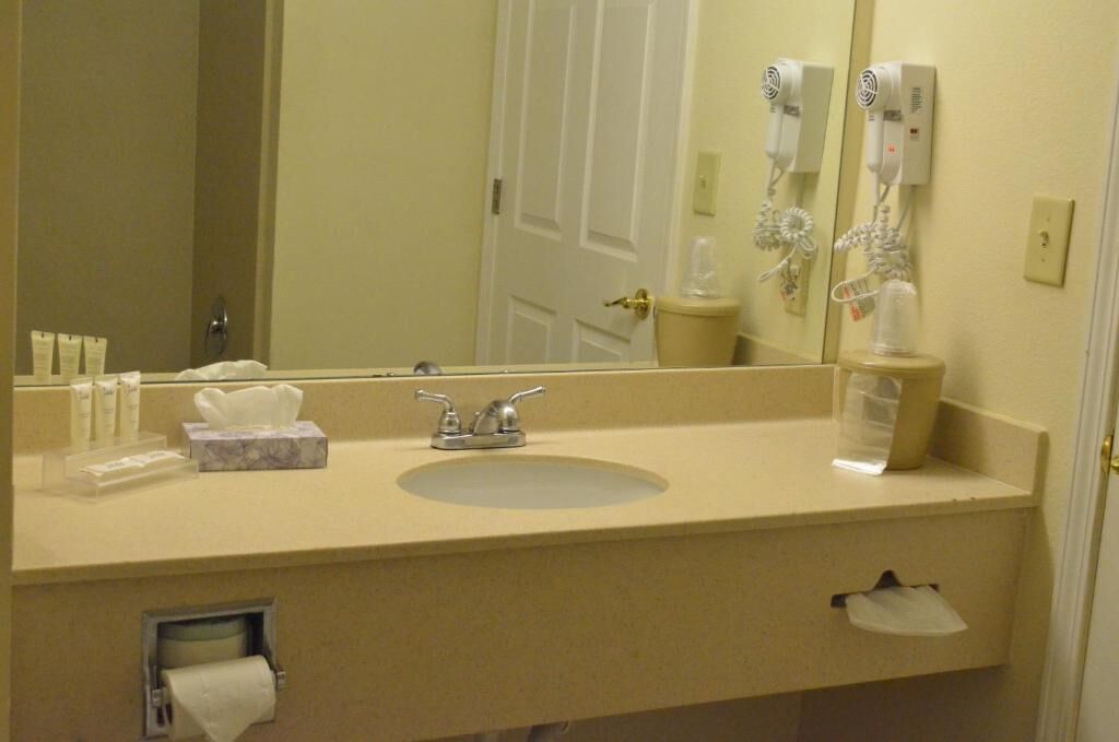 A bathroom with a sink, mirror, towel dispenser, and hair dryer.