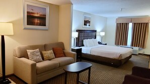 A hotel room with a bed, a sofa, a small table, a nightstand, a lamp, and a picture on the wall. - Home Inn & Suites (Montgomery)