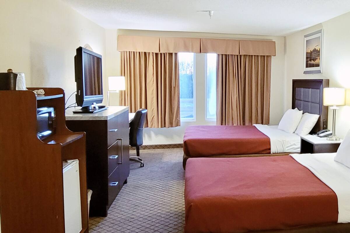 A hotel room with two beds, a desk with a computer, a TV, and a window with curtains.