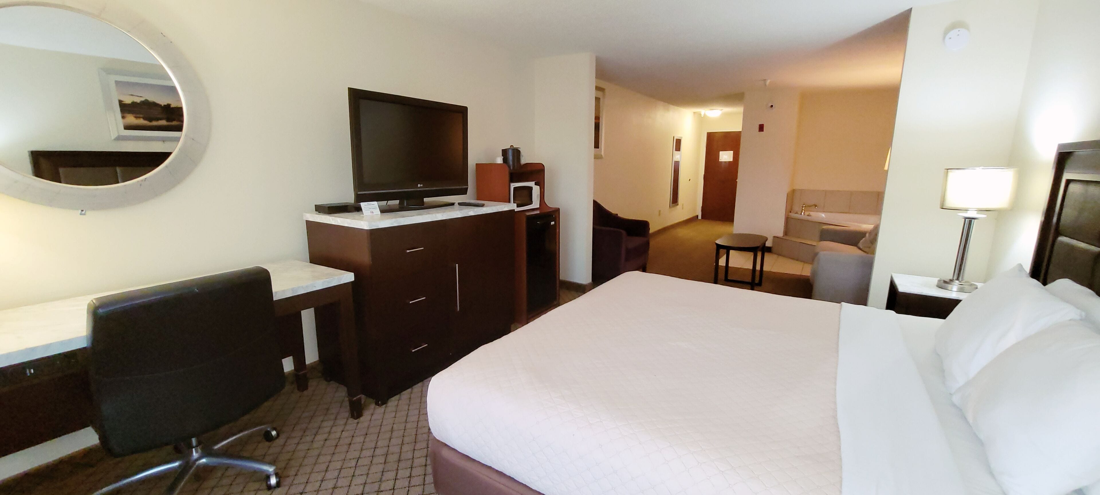 Une chambre d’hôtel comprenant un lit, un bureau avec une chaise, une télévision, un four à micro-ondes, une petite table et une lampe.