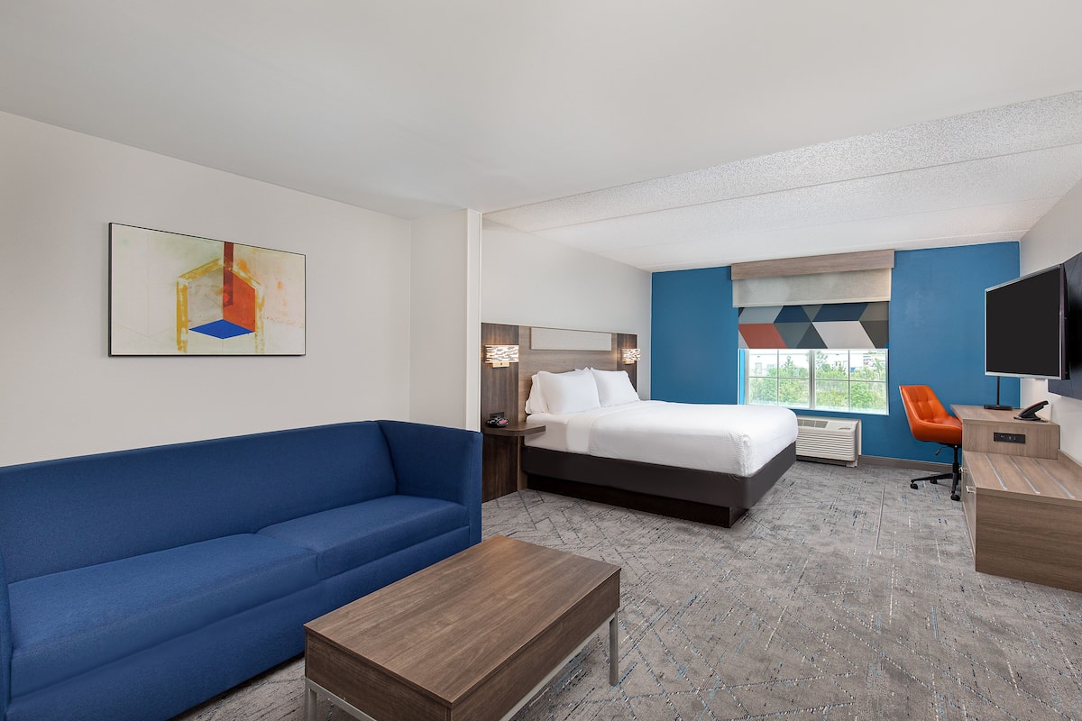 Ein Hotelzimmer mit einem Bett, einer blauen Couch, einem Holztisch und einem Bild an der Wand.