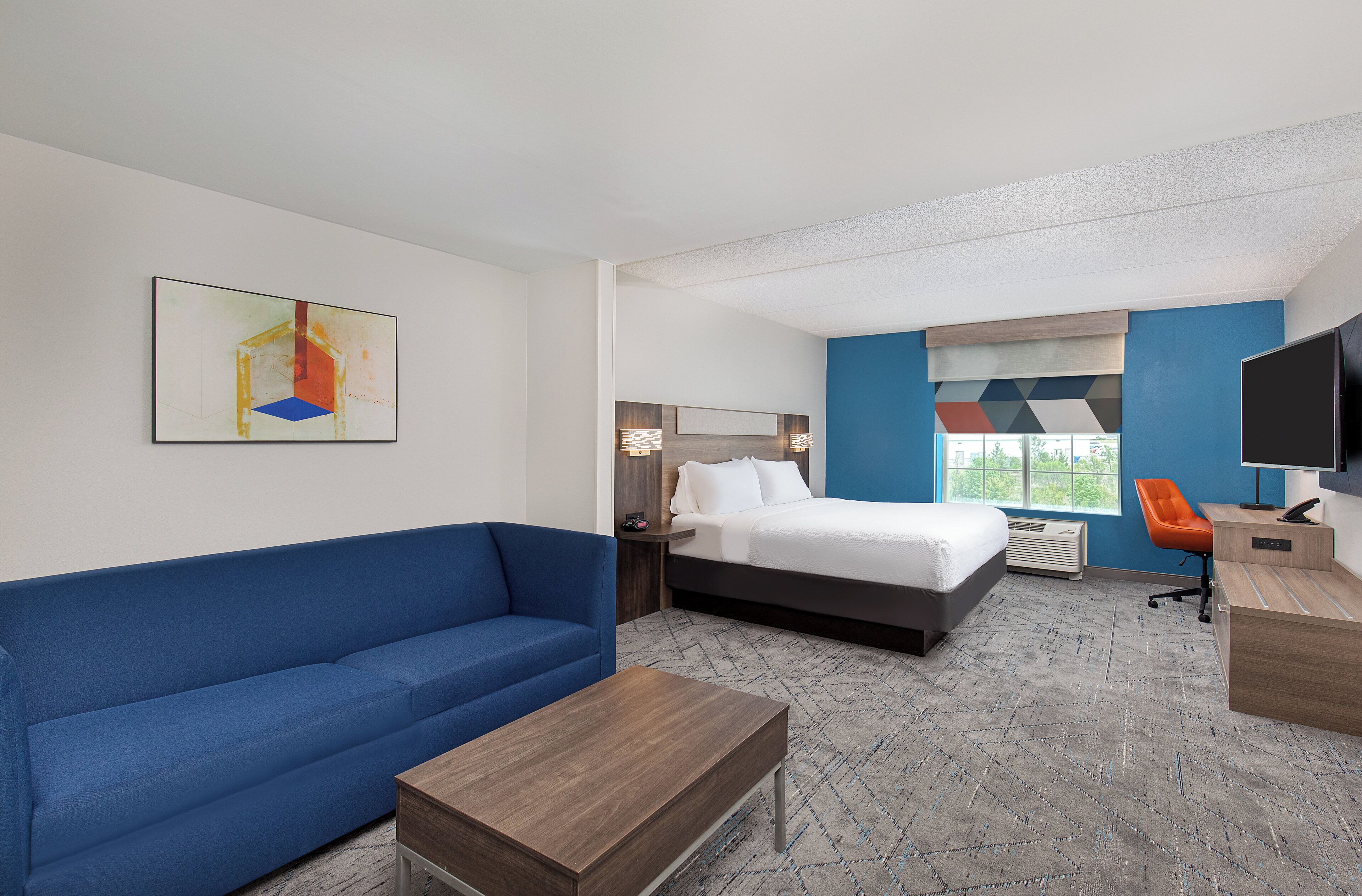 Una camera d'albergo con un letto, un divano blu, un tavolo di legno, una scrivania con un computer e una TV.