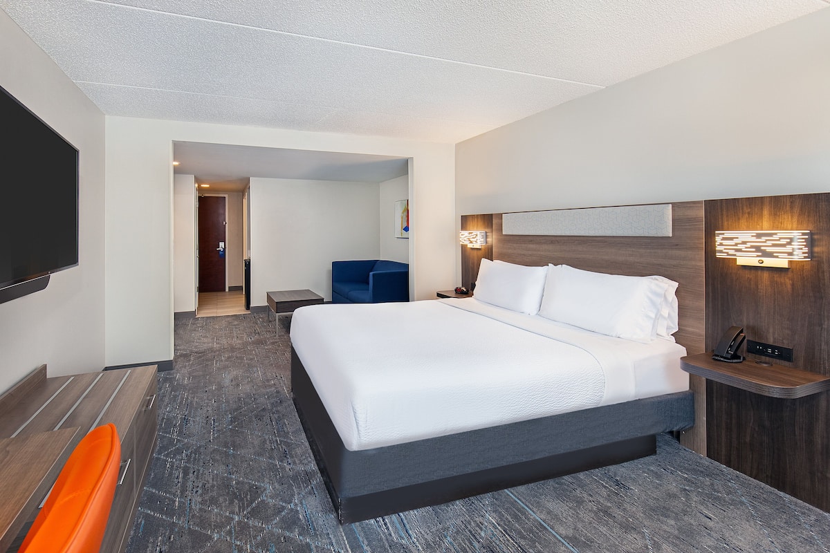 Ein modernes Hotelzimmer mit einem großen Bett, einem Fernseher, einem Schreibtisch und einem Sessel.