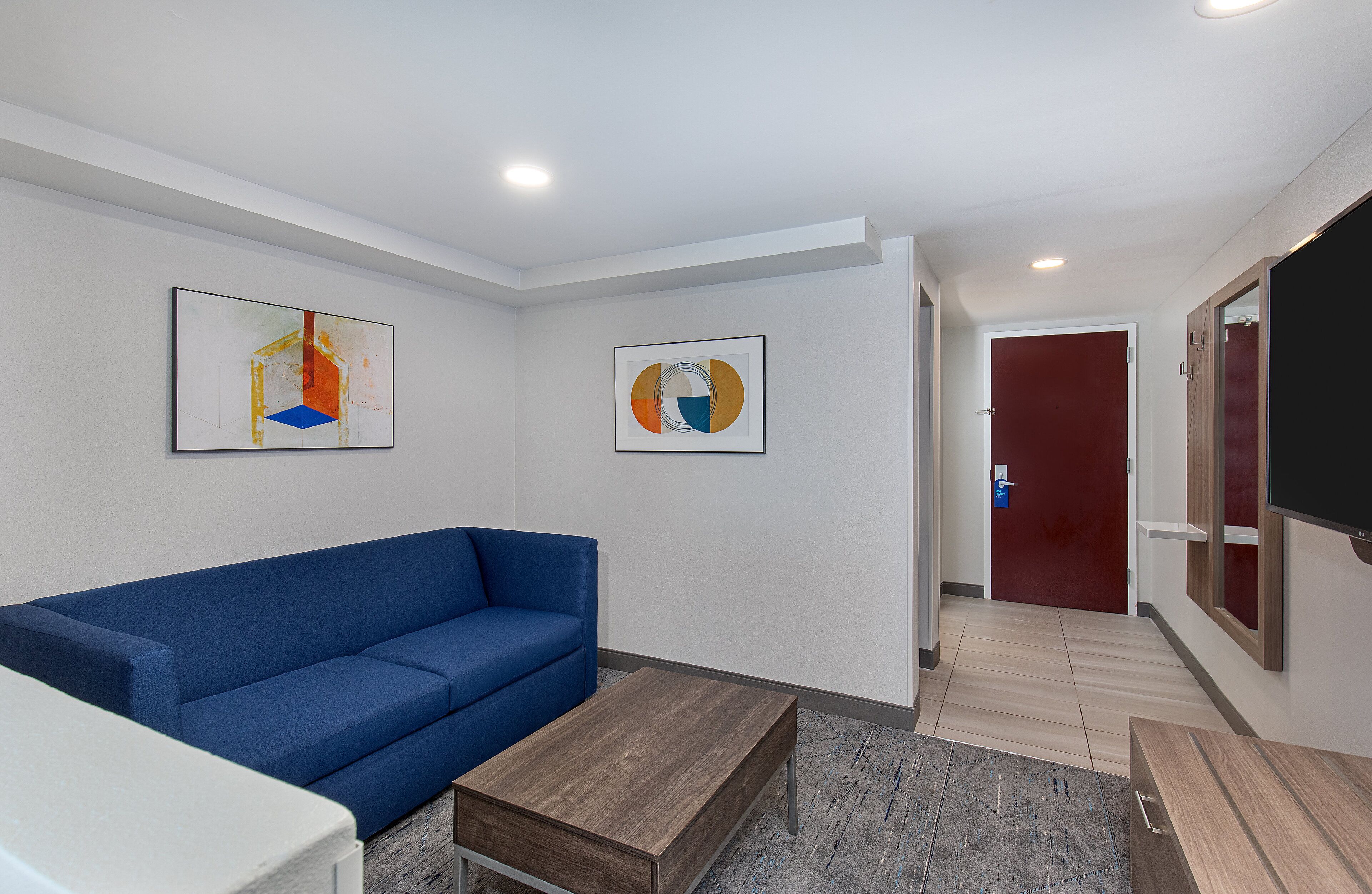 A modern waiting area with a blue sofa, a wooden coffee table, and two abstract paintings on the wall.