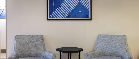 Two armchairs and a small table in a room with a geometric blue and white artwork on the wall.