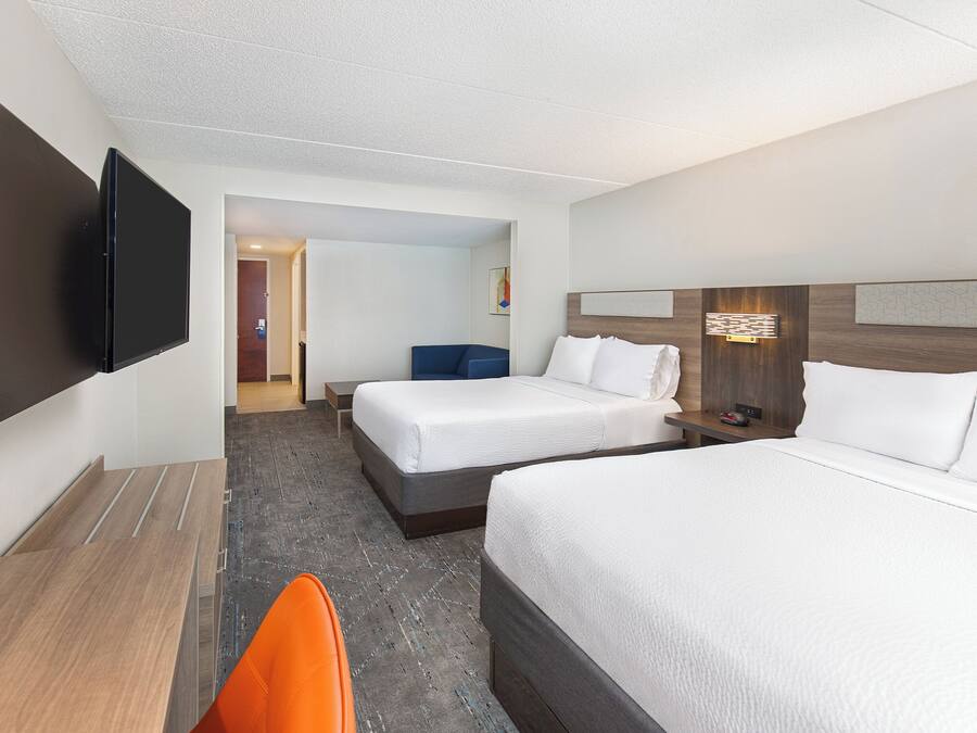 A hotel room with two beds, a desk, a chair, a flat-screen TV, and a door leading to a hallway.