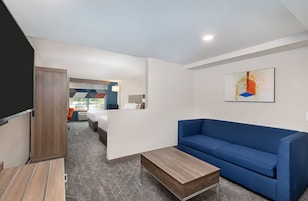 Una habitación de hotel moderna con un sofá azul, una mesa de centro de madera y un cuadro en la pared.