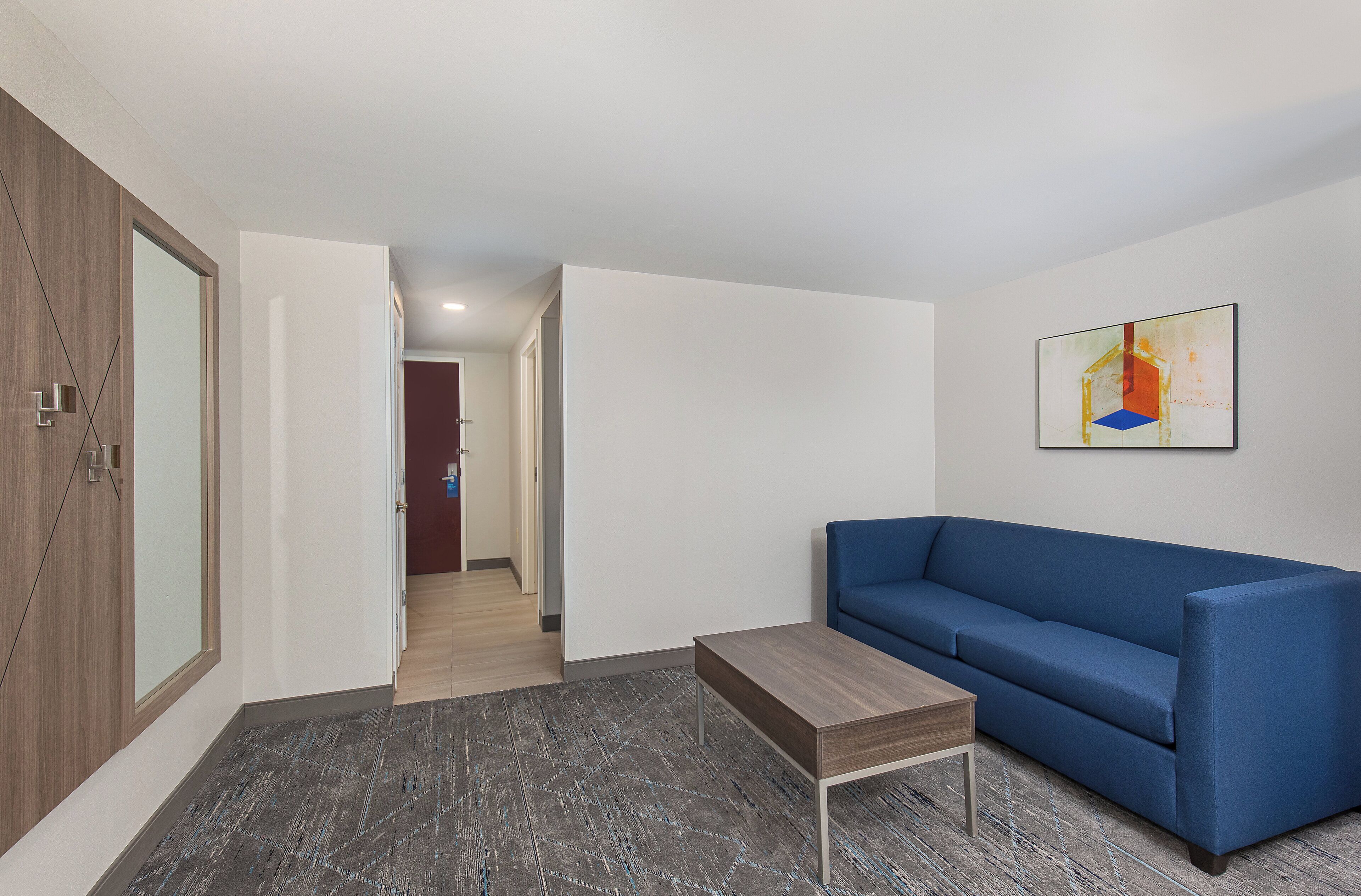 A modern living room with a blue sofa, a small wooden table, and a geometric patterned rug.