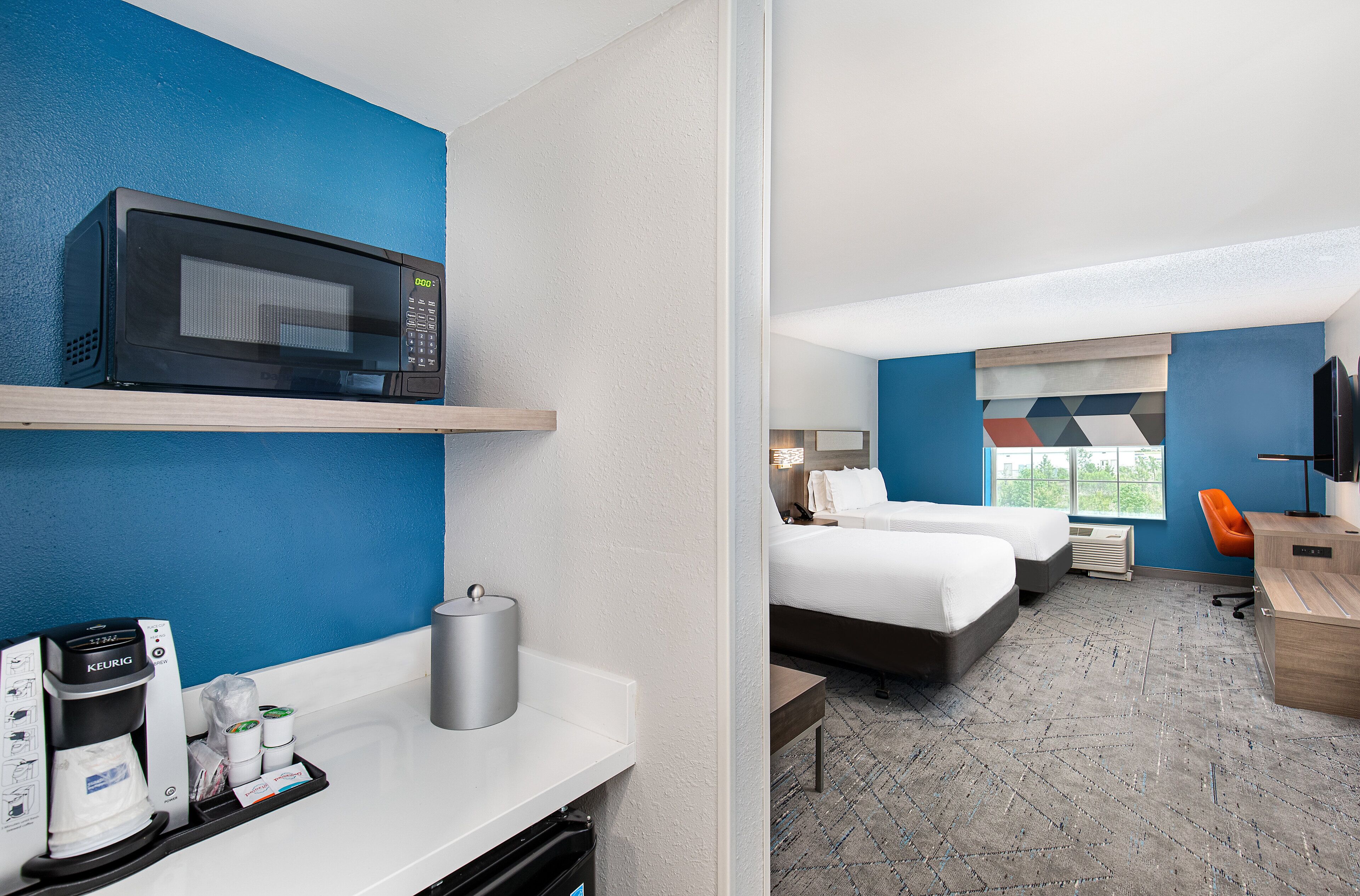 A hotel room with a kitchenette, two beds, a desk, and a TV.