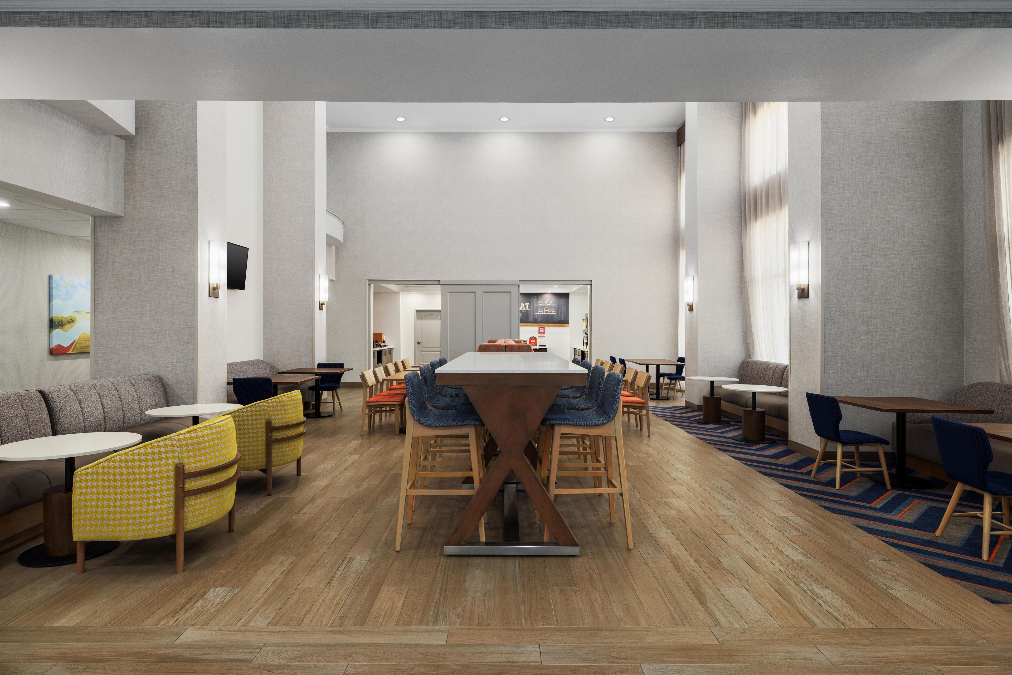 A modern dining area with a central long table, multiple seating options, and a view into the kitchen.