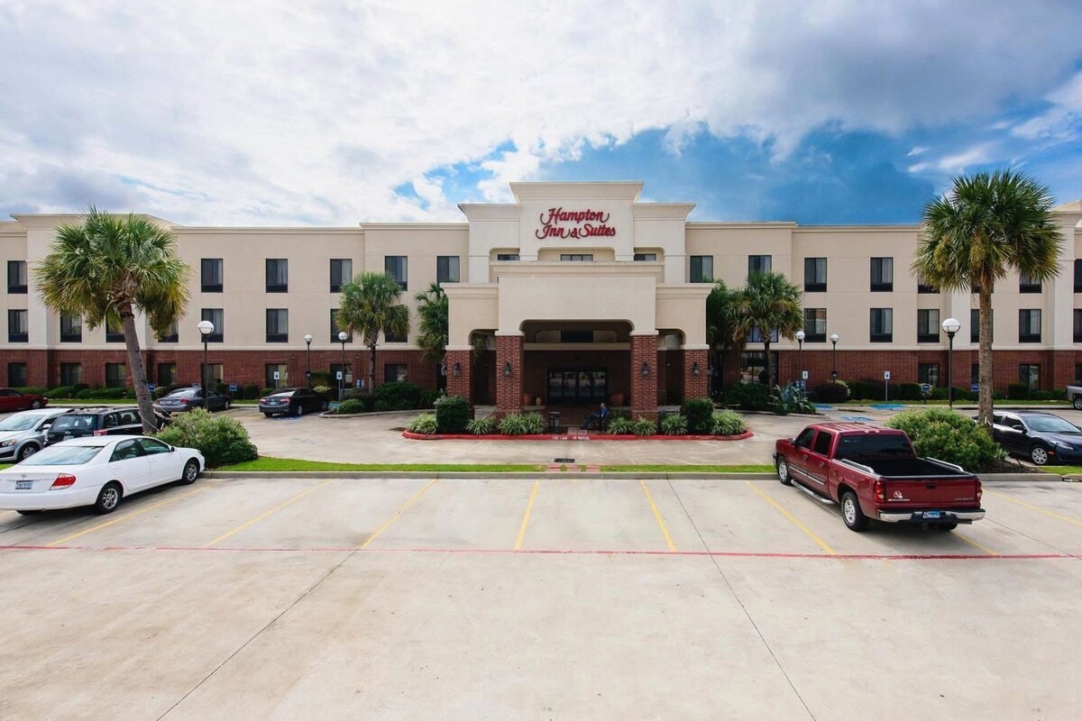 A Hampton Inn & Suites hotel with a parking lot, multiple cars, and palm trees.