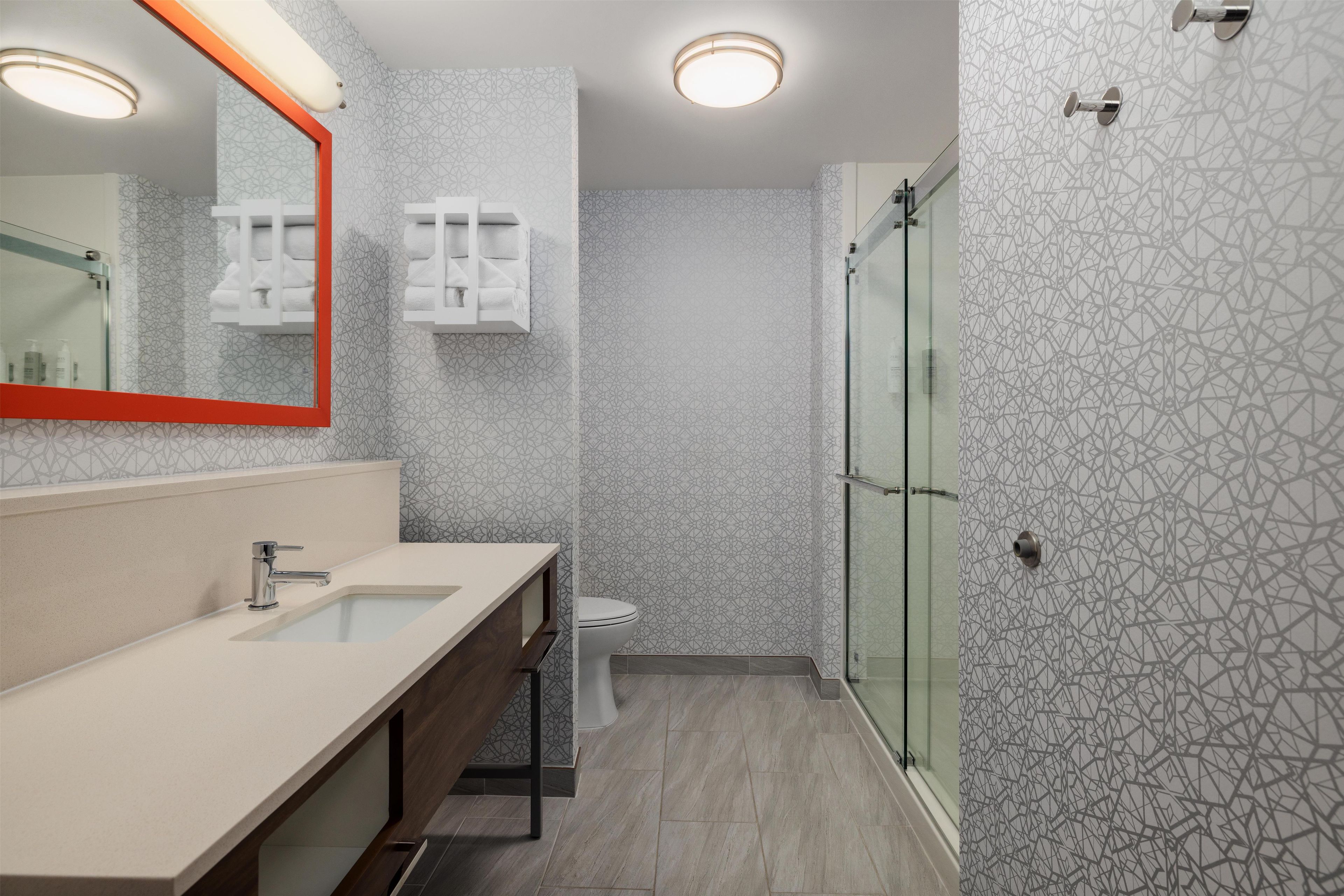 A modern bathroom with a large mirror, a sink, a toilet, and a shower area.
