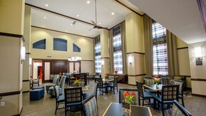 A spacious hotel dining area with multiple tables and chairs, large windows with curtains, and a ceiling fan. - Hampton Inn & Suites Port Arthur (Port Arthur)