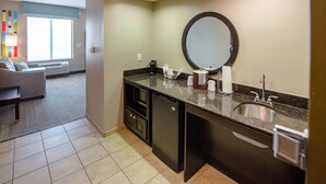 A hotel bathroom with a sink, mirror, and toiletries. There is a window with blinds and a view of the outside. - Hampton Inn & Suites Port Arthur (Port Arthur)
