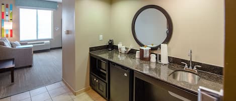 A hotel bathroom with a sink, mirror, and toiletries. There is a window with blinds and a view of the outside.