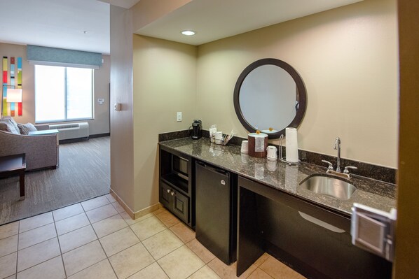 A hotel bathroom with a sink, mirror, and toiletries. There is a window with blinds and a view of the outside.
