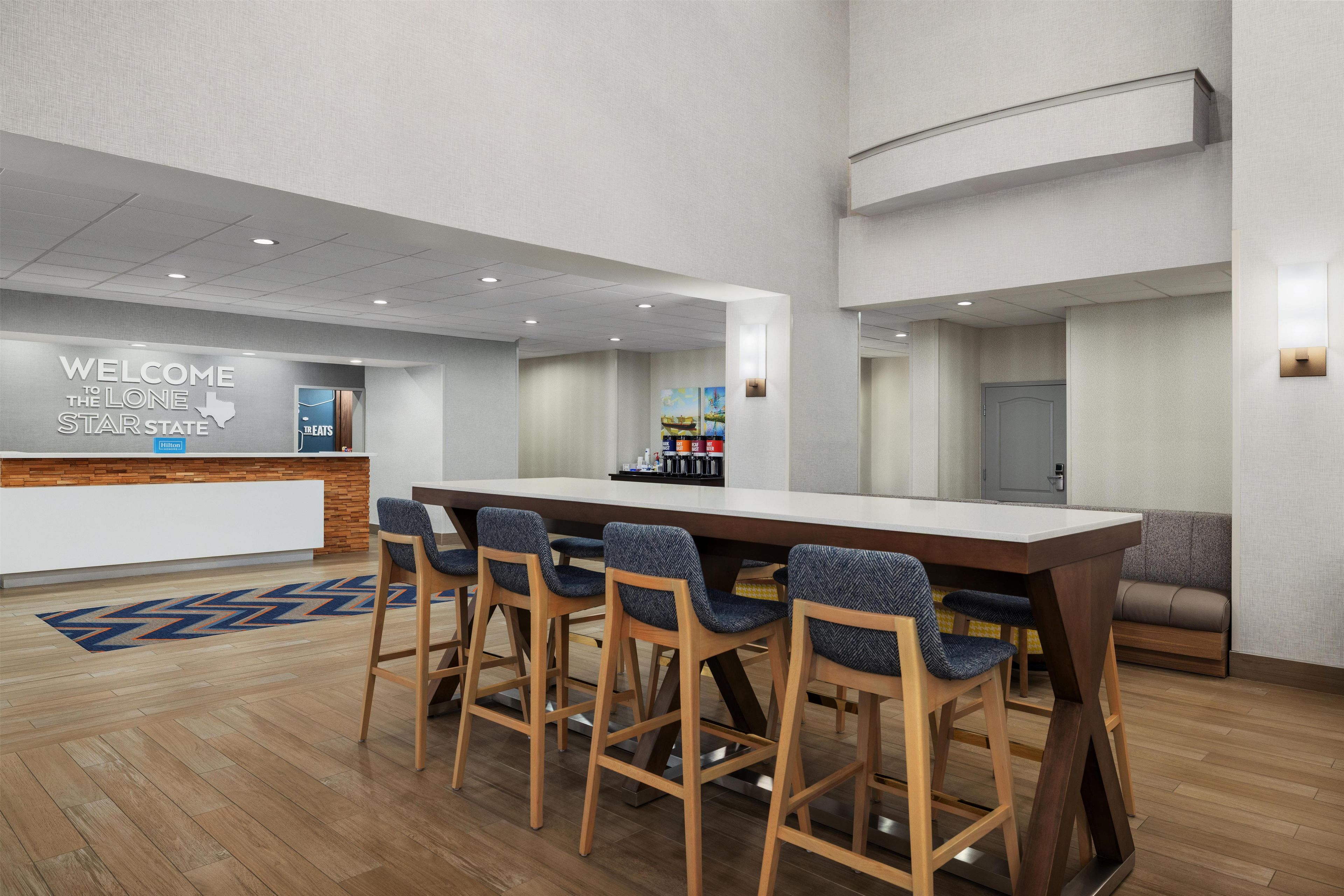A hotel lobby with a reception desk, bar area, seating, and a large wooden table.