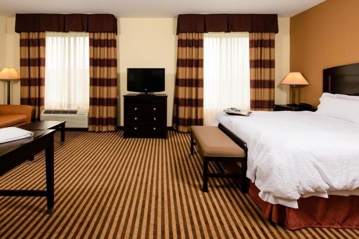 A hotel room with a bed, a desk, a chair, a television, and a lamp.